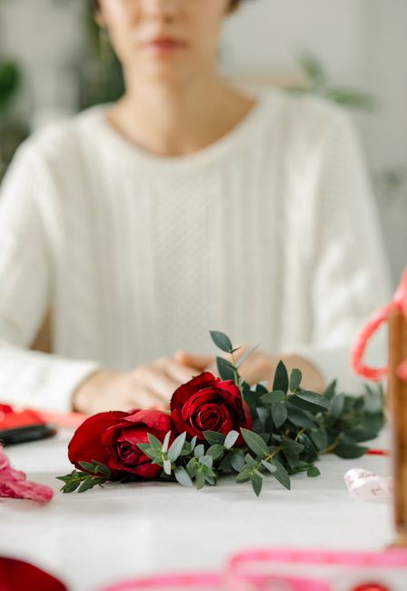 A floral arrangement featuring vibrant red roses, complemented by green eucalyptus leaves, arranged in a loose, natural style. The bouquet is placed on a white surface, with the roses partially wrappe